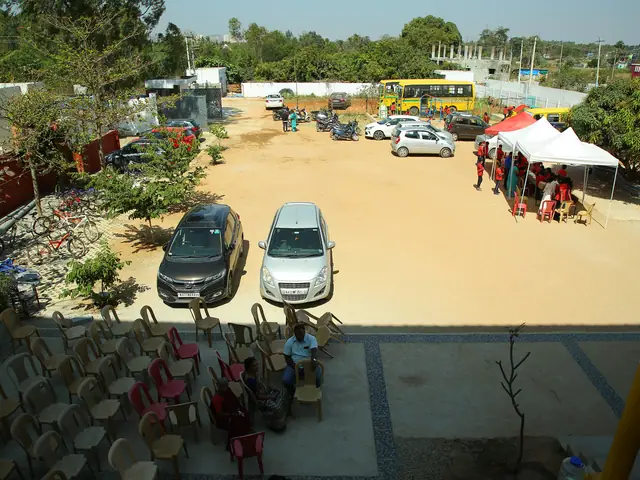 Elevated wide view across the school forecourt: parked cars, white event tents, low buildings, trees
