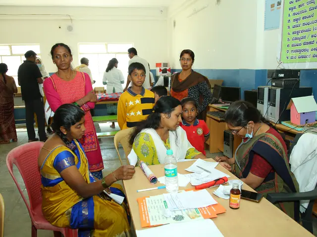 Women in bright saris and schoolgirls work at tables in a computer room with monitors and printers