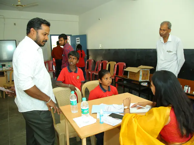 A man bends over a table where two schoolgirls and a woman are filling in papers
