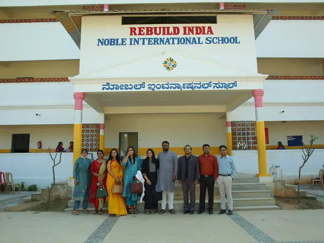 Staff and visitors in a long line in front of the main school block under the large Rebuild India sign board