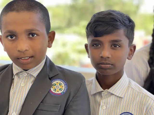 Two boys in school blazers stand shoulder to shoulder looking directly into the lens, calm and composed