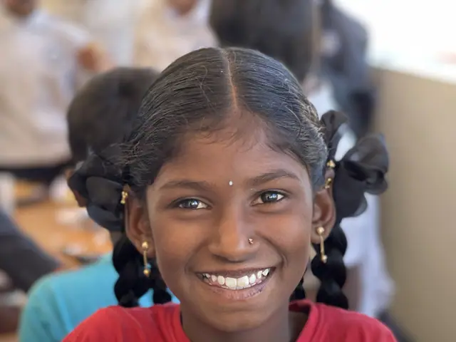 A girl holds up a large steel dish of golden fried food and laughs openly at the camera