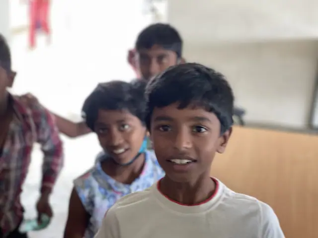 A girl and a boy in a corridor look towards the camera, the boy smiling broadly