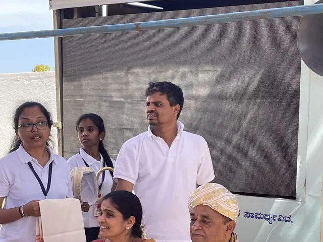 Health worker with a form beside an elderly man and a woman seated at a check-up desk