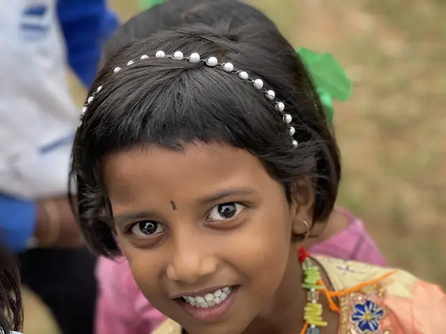 Warm chest-up portrait of a girl in an embroidered peach kurta and beaded headband, full eye contact